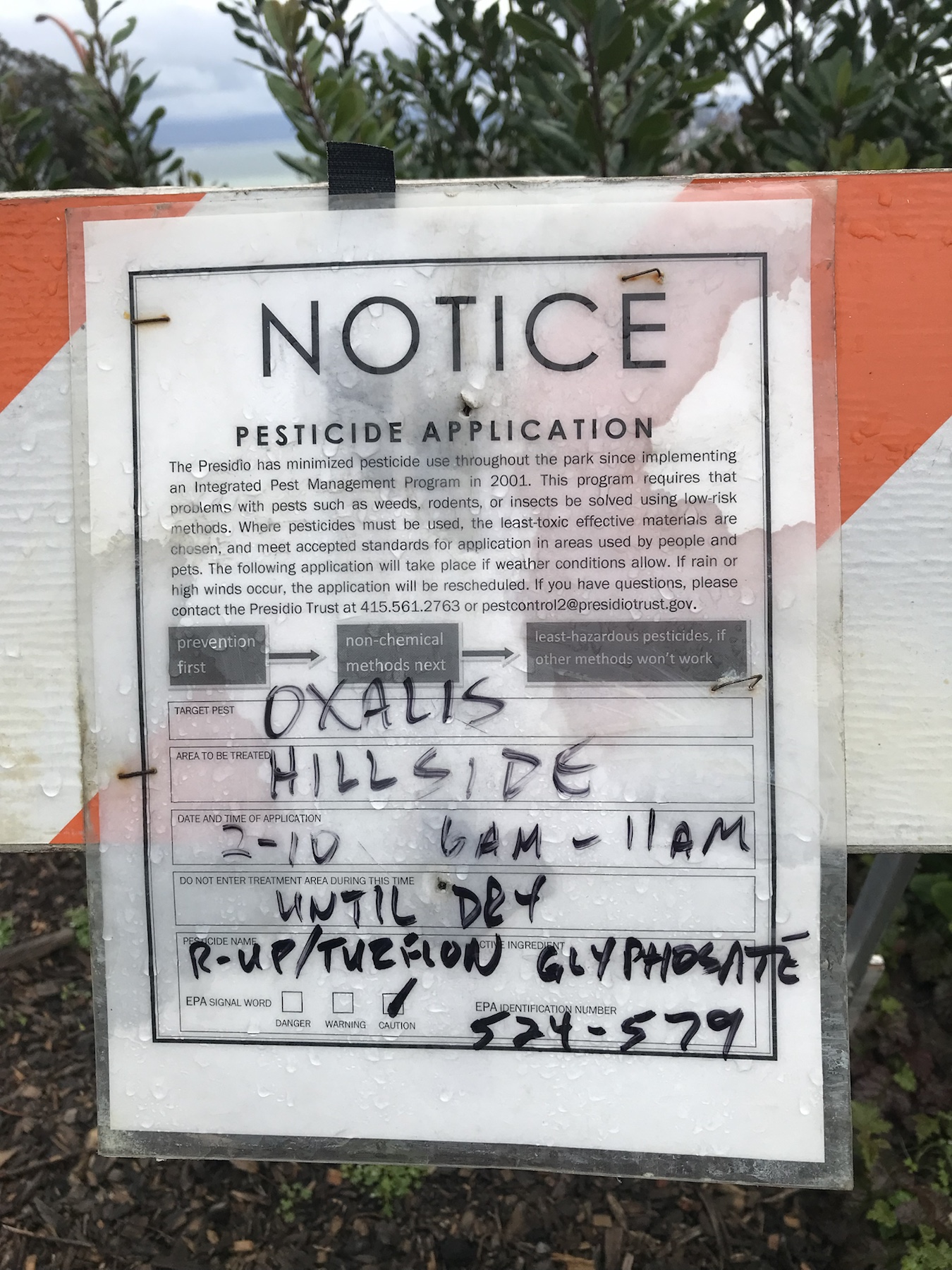 Notice pesticide application sign listing Roundup and Turflon for oxalis on a hillside