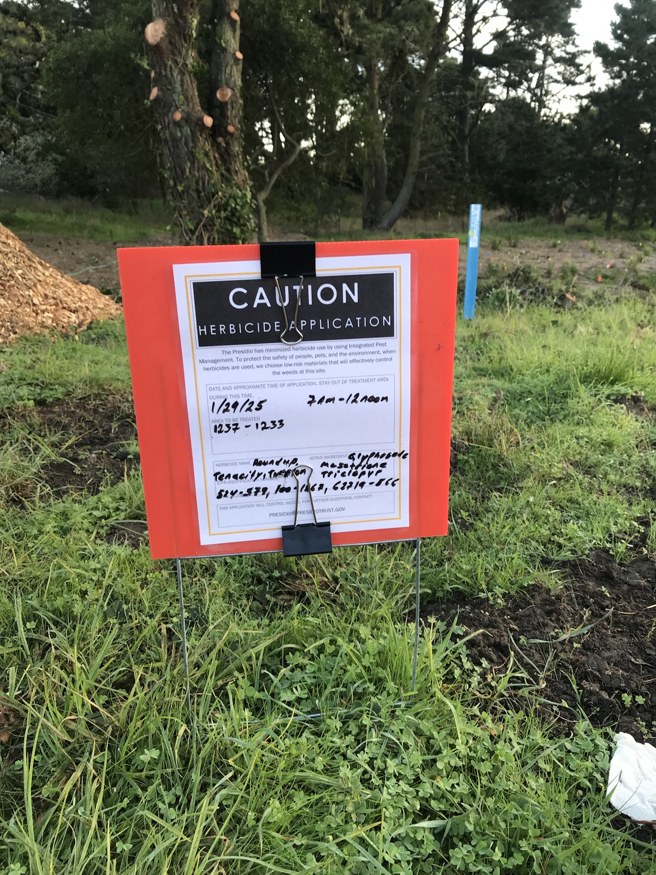 Caution herbicide application sign listing Roundup, Tenacity, and Turflon near buildings 1233 to 1237