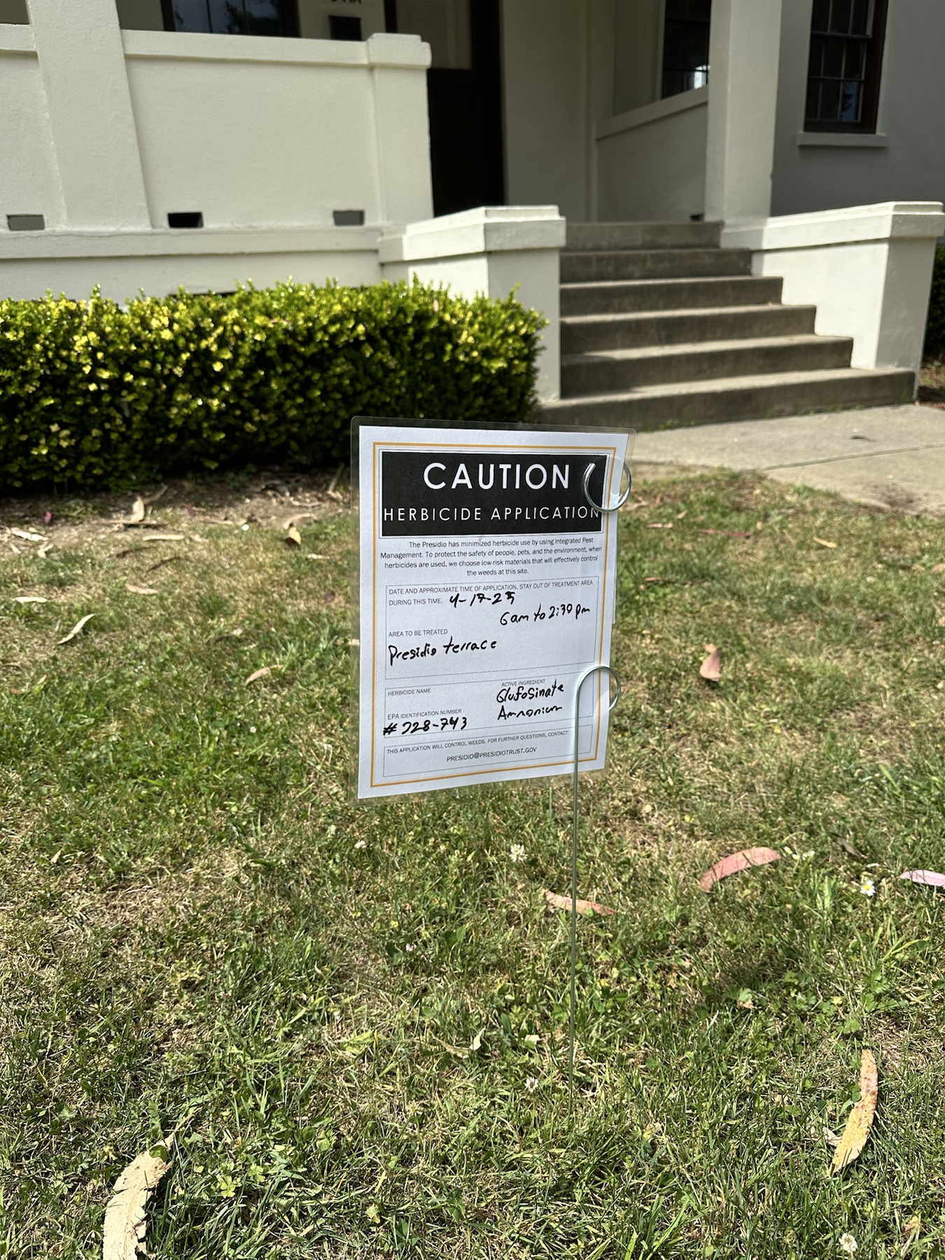 Wider context image of a herbicide application sign posted in a lawn area at Presidio Terrace
