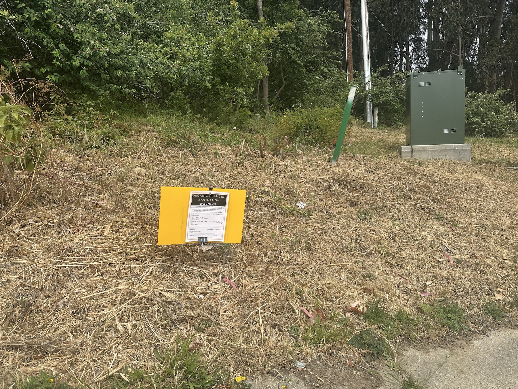 Context image of an organic herbicide application sign on a dry slope near utility equipment