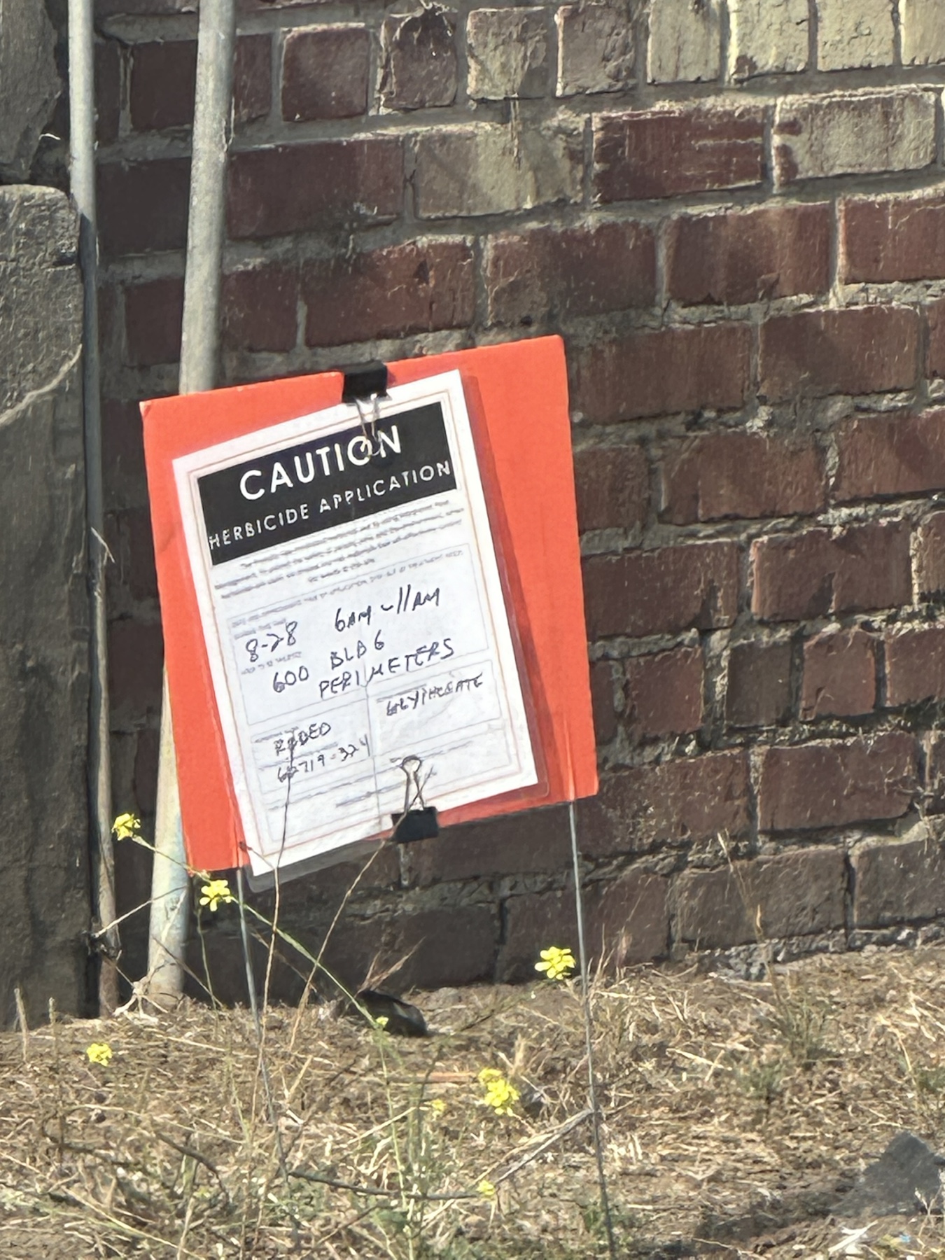 Caution herbicide application sign listing Rodeo and glyphosate for Building 663 perimeters